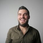 Portrait of a bearded man smiling joyfully in a casual studio setting.