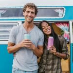 Smiling couple standing by a blue camper van, enjoying their travel adventure.